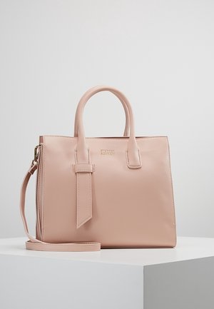 Lachsrosa Ledertasche mit doppelten Griffen, abnehmbarem Schulterriemen und dezentem goldfarbenem Markenlogo vorne, präsentiert auf einem weißen Podest.