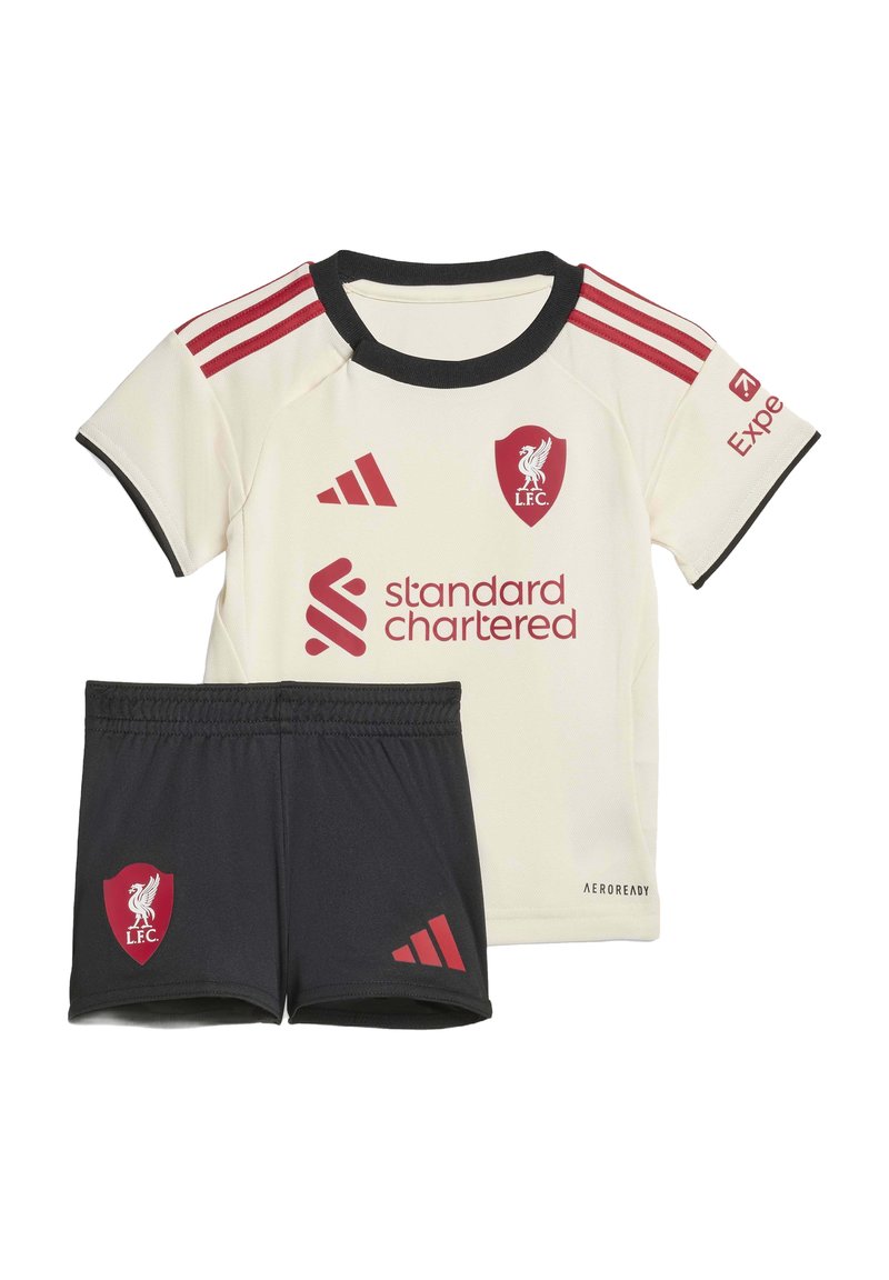 Liverpool FC kids’ soccer kit with cream shirt featuring red logos and black shorts displaying red Liverpool crest and Adidas logo.