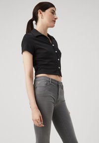 Top negro corto con botones, de manga corta y botones plateados, combinado con jeans ajustados grises. Diseño sencillo y textura suave.