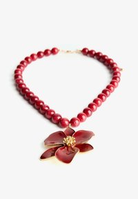 Röd pärlhalsband med en stor röd blompendant med gyllene detaljer i mitten och släta, glänsande ytor.