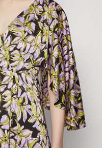 Φλοράλ φόρεμα με μοτίβο μωβ και πράσινα λουλούδια σε μαύρο φόντο. Περιλαμβάνει φαρδιές, ναξερές μανίκες και V-λαιμόκοψη.