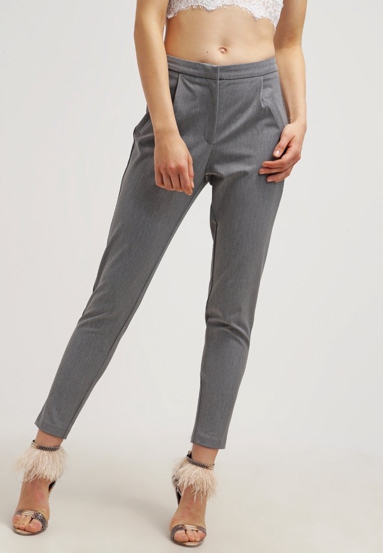Pantalon gris ajusté en tissu texturé, avec poches latérales, taille haute et jambes fuselées. Associé à des sandales à talons duveteuses.