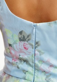 Vaaleansininen kukkamekko, jossa on vaaleanpunaisella ja vihreällä kukkakuvio. Mekossa on takana vetoketjusuljenta ja sileä, teksturoitu kangas.