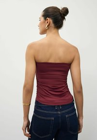 Burgundy bezpiedurkņu topi ar ručotām detaļām aizmugurē, apvienots ar tumšiem džinsiem. Gluda auduma, pieguļošs dizains un bez redzamām rakstāmzīmēm.