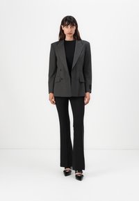 Dvouřadový šedý pruhovaný blazer s širokými klopami, spárovaný s černými upnutými kalhotami a černými lodičkami s špičatou špičkou.