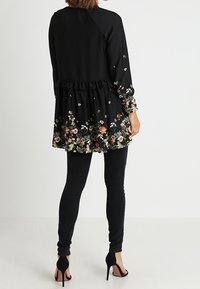 Svart tunika med blommönster vid fållen, volang i midjan och långa ärmar. Matchas med svarta skinny jeans och klackar.