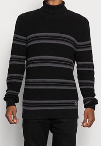 Maglione nero a collo alto con strisce orizzontali grigie, texture a costine e maniche con polsini. Presenta una toppa con logo all'orlo.