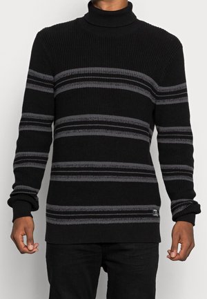 Suéter de cuello alto negro con rayas horizontales grises, textura acanalada y mangas con puños. Presenta un parche de logo en el dobladillo.