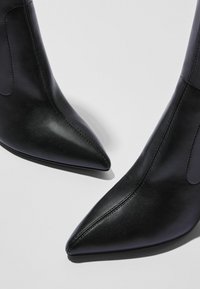 Svarta läderankelstövlar med spetsig tå, slät yta och diskreta sömmar på skaftet.