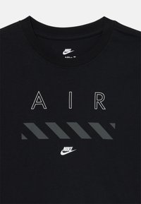 Fekete pamut póló, amelyen fehér betűkkel "AIR" felirat és szürke diagonális csíkok találhatók. A Nike logó fehér színben, a felirat alatt helyezkedik el.