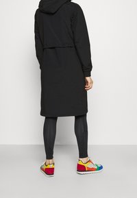 Svart vattentät jacka med huood, med en kortad design, kombinerad med smala svarta leggings och flerfärgade sneakers med abstrakta mönster.