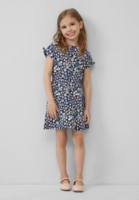 Blumenkleid mit navy-blauem Hintergrund und bunten Blumen, kurzen Ärmeln mit Rüschendetails, tailliertem Bund und ausgestelltem Rock; kombiniert mit rosa Schuhen.