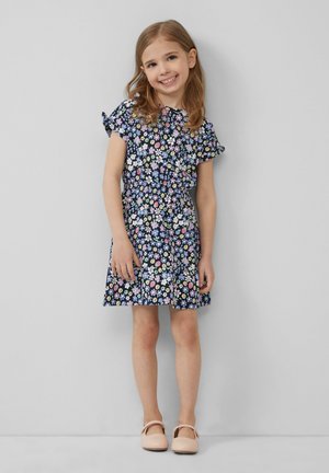 Blumenkleid mit navy-blauem Hintergrund und bunten Blumen, kurzen Ärmeln mit Rüschendetails, tailliertem Bund und ausgestelltem Rock; kombiniert mit rosa Schuhen.