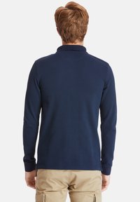 Mörkblå långärmad polo med ribbat mönster och klassisk krage. Har åtsittande ärmar och rak nederkant.