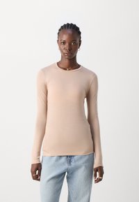 Langermet, tettsittende topp i lys beige, laget av glatt stoff. Rund halslinning med noe forlengede ermer, kombinert med lys denim.