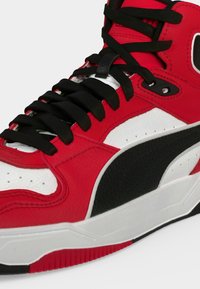 Κόκκινο, λευκό και μαύρο sneaker ψηλής κορυφής με μαύρα κορδόνια, υφασμένο μαύρο σχέδιο στο πλάι και παχύ λευκό πέλμα.