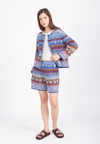 Komplet z marynarką i szortami w wzory z niebieskimi, pomarańczowymi i białymi kwiatami, teksturowany sweter i brązowe sandały.