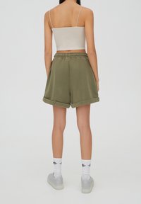 Pantalones cortos de algodón verde oliva con dobladillo vuelto, cintura elástica y corte relajado. Combinados con calcetines blancos y zapatillas grises.