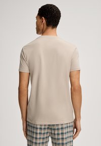 Beige bomulds T-shirt med rund hals og korte ærmer, der har en glat tekstur. Sammen med ternede shorts i blå, grøn og hvid.