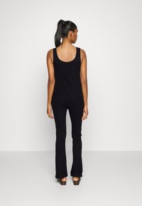 Macacão preto canelado com costas em forma de scoop, silhueta ajustada e calças largas, combinado com sapatos de salto grosso.