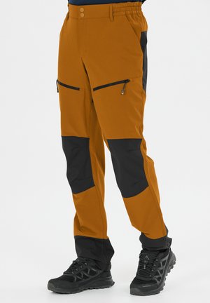 Bruine en zwarte wandelbroeken voor heren met ritssluitingen op de dijen, verstevigde knieën en een elastische tailleband, gedragen met zwarte trailschoenen.