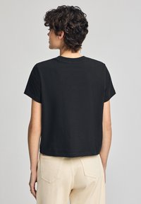 Svart bomull t-shirt med korta ärmar, rundad hals och cropped design, med en mjuk textur och minimalistisk stil.