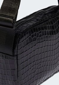 Črna torbica z usnjeno teksturo krokodila in zadrgo, ki ima trpežen trak in eleganten pravokoten obliko.