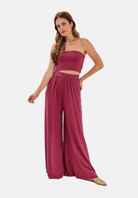 Dvoudílný outfit zahrnuje top bez ramínek a kalhoty s širokými nohavicemi v bohaté burgundské tkanině. Měkká textura s elastickým pasem.