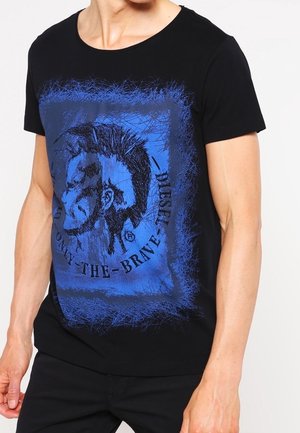 Mann, der ein schwarzes T-Shirt mit einer blauen Grafik eines stachelhaarigen Gesichts und dem Text "Only The Brave Diesel." trägt