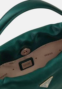 Zielona satynowa torebka od środka z beżową podszewką. Posiada metkę z logo oraz metalowe zapięcie na zatrzask. Logo widoczne na podszewce.