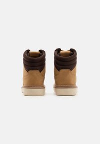 Botas de ante marrón a la altura del tobillo con cuellos de tejido marrón acolchados, suelas de goma beige y detalles de costura en contraste en los bordes.