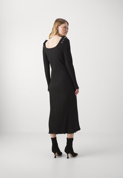 Rochie neagră cu mâneci lungi și textură în dungi, cu spatele decupat, având accente cu volane pe umeri și o linie de jos care se termină puțin sub genunchi.