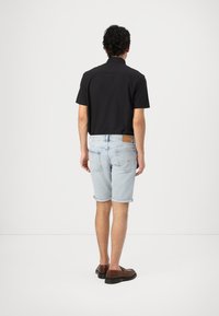 Camisa negra de manga corta, pantalones cortos de mezclilla azul claro con dobladillos enrollados y zapatos marrones. Diseño simple con acentos y texturas mínimas.