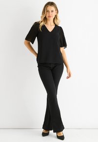 Black top with a V-neck and pleated sheer sleeves, paired with black flared jeans and black pointed-toe shoes.