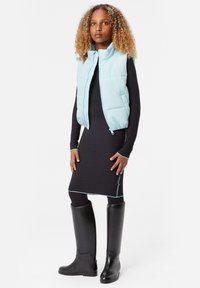 Ljusblå puffer väst med dragkedja framtill, kombinerad med en svart ribbad klänning och knähöga svarta stövlar. Har kontrasterande sömmar.