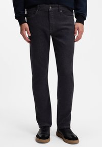 Jeans de mezclilla gris oscuro con corte recto, con cinco bolsillos, costuras sutiles y cierre clásico de botón. Zapatillas negras y marrón claro.