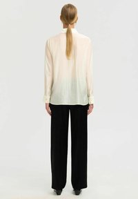 Lange mouwen, lichtbeige shirt met een relaxte pasvorm, knoopmanchetten en een licht doorzichtige textuur, gecombineerd met hoge zwarte broeken.