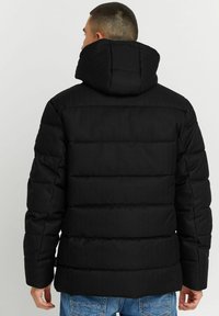 Schwarze Steppjacke mit Kapuze, gestepptem Design und strukturierter Oberfläche. Sichtbare Nähte und ein sicherer Sitz an der Taille.
