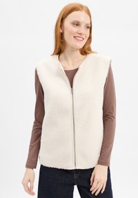 Weißer Fleece-Weste mit hohem Kragen und einem Reißverschluss vorne; getragen über einem braunen Langarmshirt; der Hintergrund ist schlicht weiß.