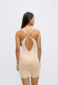 Ādas krāsas pieguļošs bodijs ar apaļu muguras izgriezumu, regulējamām krustiņveida lencēm un gludu faktūru, kas stiepjas līdz vidus augšstilbam.