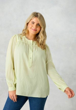 Blusa verde chiaro con maniche lunghe, scollatura rotonda, parte anteriore plissettata e pattina con bottoni. Realizzata in un tessuto morbido e leggero.