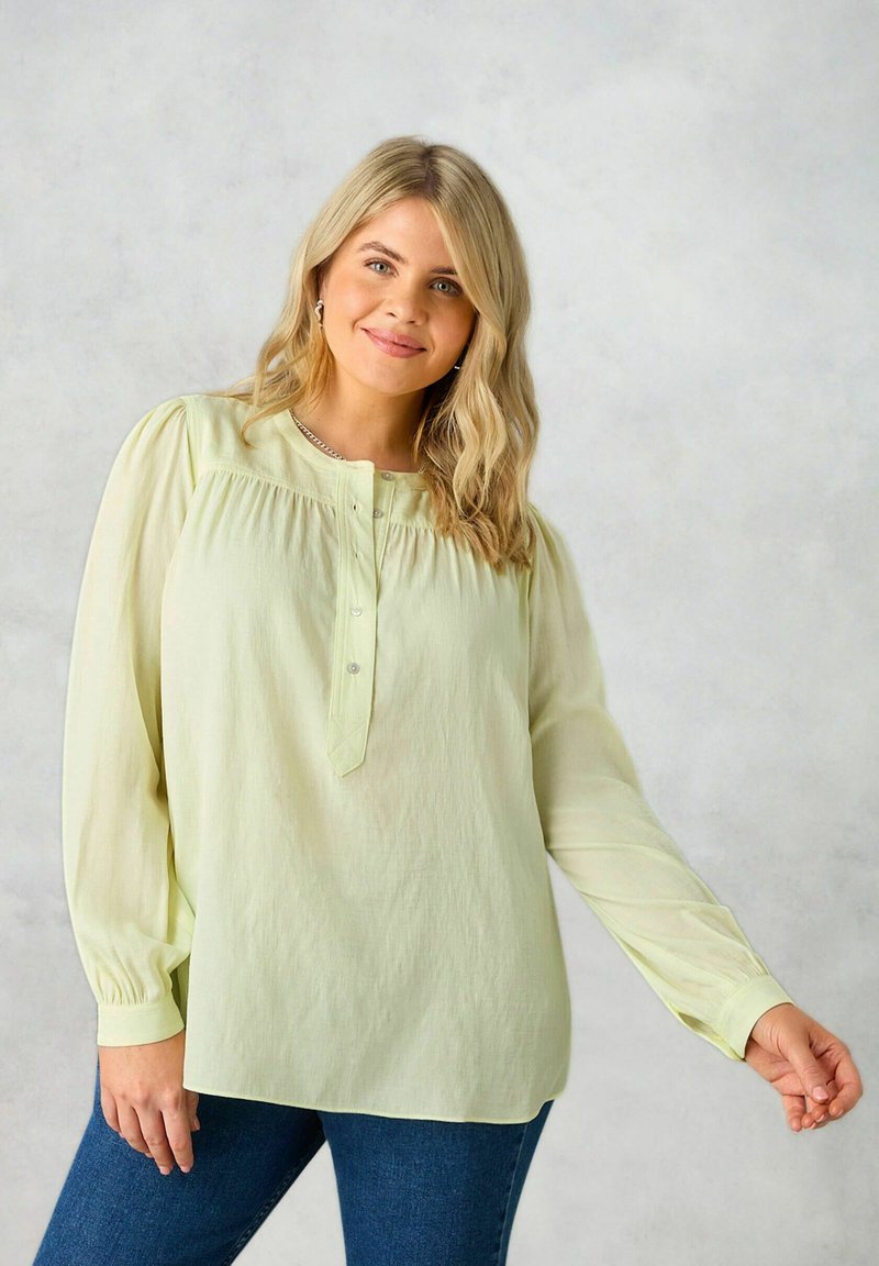 Blusa verde chiaro con maniche lunghe, scollatura rotonda, parte anteriore plissettata e pattina con bottoni. Realizzata in un tessuto morbido e leggero.