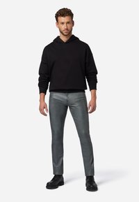 Zwart hoodie met een losse pasvorm, gecombineerd met slim-fit grijze broek van een glad, glanzend materiaal. Model draagt zwarte veterschoenen.