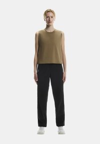 Hnedý top bez rukávov s voľným strihom, v kombinácii s čiernymi nohavicami rovného strihu. Topánky sú v bielej športovej kvalite. Jednoduchý dizajn, bez vzorov.