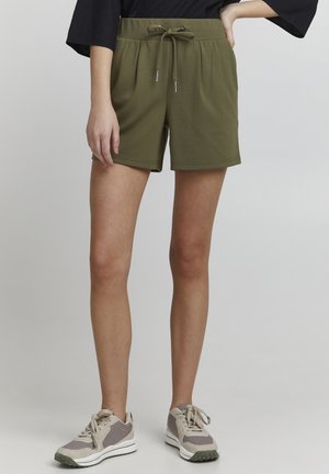 Olive green shorts made of soft fabric, featuring an elastic waistband with a drawstring and rolled hem. Paired with beige athletic shoes.