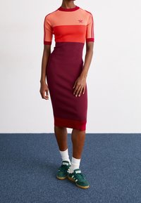 Tröja i midi-längd med ribbad textur, i färgerna orange, röd och mörkröd med färgblockering, korta ärmar och rund halsringning.