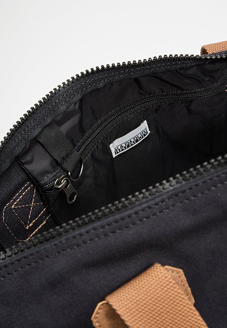 Binnenkant van een zwarte stoffen tas met een ritszak, zwarte rits, beige handvat en een wit Napapijri merklabel dat van binnen is genaaid.
