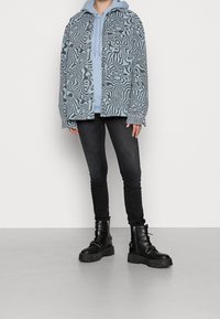 Chaqueta de camisa de color azul claro con un patrón sobre una sudadera con capucha de color azul claro, combinada con unos jeans ajustados negros y botas de tobillo negras con cordones y suelas gruesas.