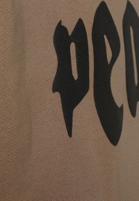 Tela beige con texto estilizado en negro. La textura parece suave, con un patrón de punto fino. No se presentan detalles visuales adicionales.
