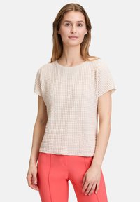 Light beige textured top with a crew neckline and short sleeves, featuring a subtle grid pattern. Paired with coral fitted pants.
